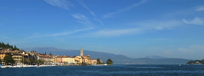 Trip Island beliebte Urlaubsziele am Gardasee -  Mit einer Fläche von 370 km² ist der Gardasee der größte See Italiens. Es liegt am Fuße der Alpen und erstreckt sich über drei Staaten: Lombardei, Venetien und Trentino. Die maximale Tiefe des Sees beträgt 346 m, er hat eine längliche Form und sein nördliches Ende ist sehr schmal. Dort ist der See von den Bergen der Gruppo di Baldo umgeben. Du trittst aus deinem gemütlichen Hotelzimmer und es begrüßt dich die warme italienische Sonne. Du blickst auf den atemberaubenden Gardasee, der in zahlreichen Blautönen schimmert - von tiefem Dunkelblau bis zu funkelndem Türkis. Majestätische Berge umgeben dich, während die Brise sanft deine Haut streichelt und der Duft von blühenden Zitronenbäumen deine Nase kitzelt. Du schlenderst die malerischen, engen Gassen entlang, vorbei an farbenfrohen, blumengeschmückten Häusern. Vereinzelt unterbricht das fröhliche Lachen der Einheimischen die friedvolle Stille. Du fühlst dich wie in einem Traum, der nicht enden will. Jeder Schritt führt dich zu neuen Entdeckungen und Abenteuern. Du probierst die köstliche italienische Küche mit ihren frischen Zutaten und verführerischen Aromen. Die Sonne geht langsam unter und taucht den Himmel in ein leuchtendes Orange-rot - ein spektakulärer Anblick.